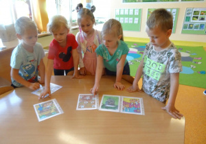 Dzieci przyglądają się ilustracją rozłożonym na stole.